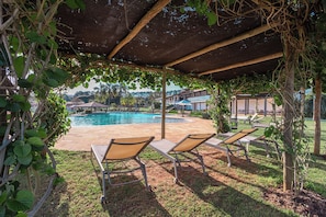 A poolside area with lounge chairs, a covered patio, and a view of buildings in the background.