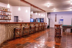 Zona de bar con una barra larga, varias sillas, mesa de billar y televisor.