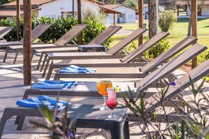 Un área junto a la piscina con sillas de descanso y una mesa con bebidas.