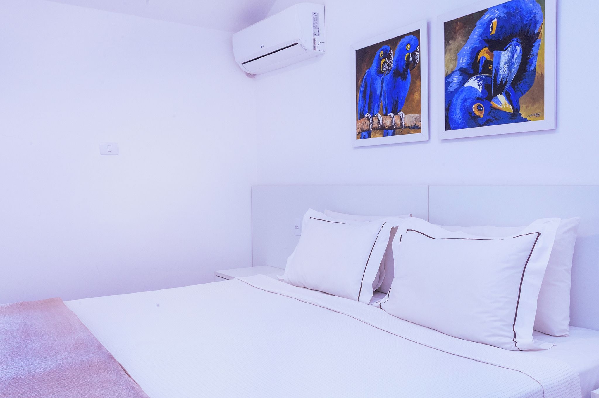 Ein Schlafzimmer mit einem Bett, weißer Bettwäsche, einer Klimaanlage und zwei Bildern an der Wand.
