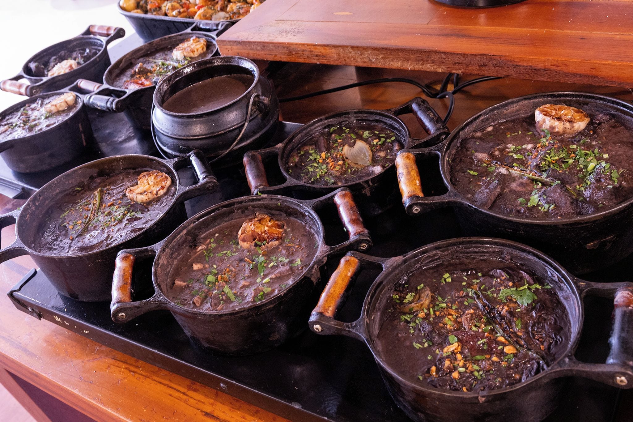 A kitchen with multiple cast iron skillets on a stove, some containing food.