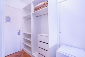 Un placard blanc avec des étagères et des tiroirs, une tringle pour suspendre les vêtements et une serviette pliée posée sur le dessus.