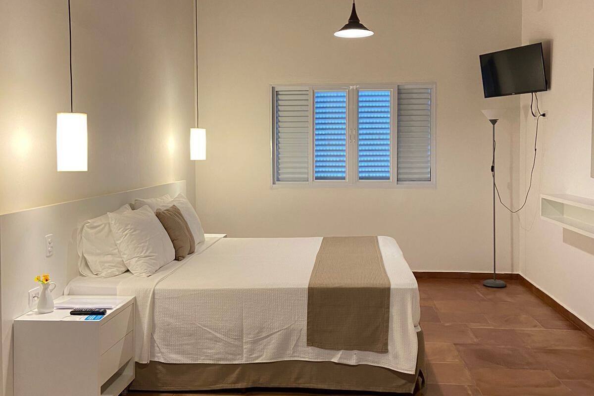 Une chambre à coucher comprenant un lit, une table de chevet, une lampe, un téléviseur et un appareil de climatisation.