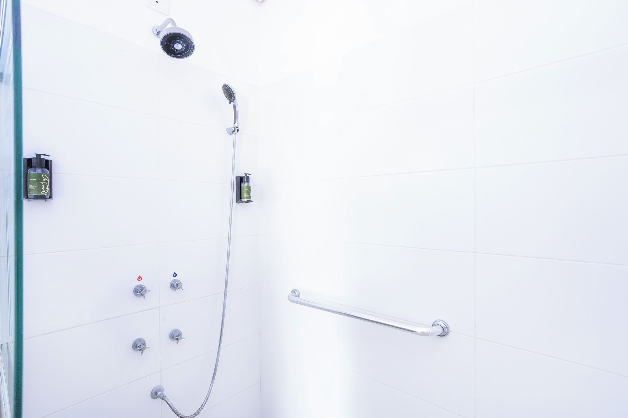 A shower area with a handheld showerhead, a wall-mounted control panel, and a grab bar.