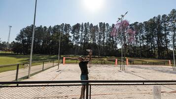 Una cancha de tenis con red, rodeada de una cerca y árboles al fondo.