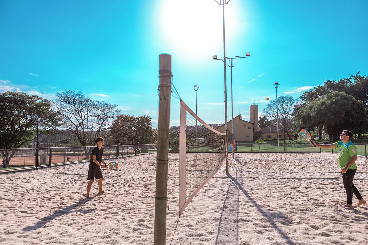 Una cancha de voleibol con una red, rodeada por una cerca y árboles al fondo.