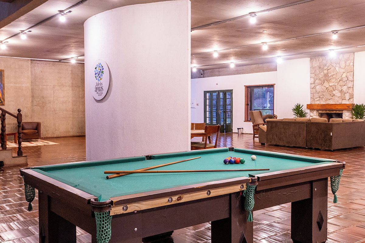 A pool table in a room with a stone fireplace, a wooden bench, and a view of the outdoors.
