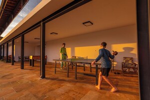A spacious indoor area with a ping pong table, a wooden floor, and a large window allowing natural light.