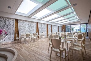 A spacious dining area with high ceilings and skylights, featuring modern furniture and a central decorative element. - Hotel Quisisana (Abano Terme)