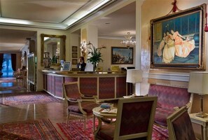 A lobby with a reception desk, seating area, and a large painting on the wall. - Hotel Quisisana (Abano Terme)