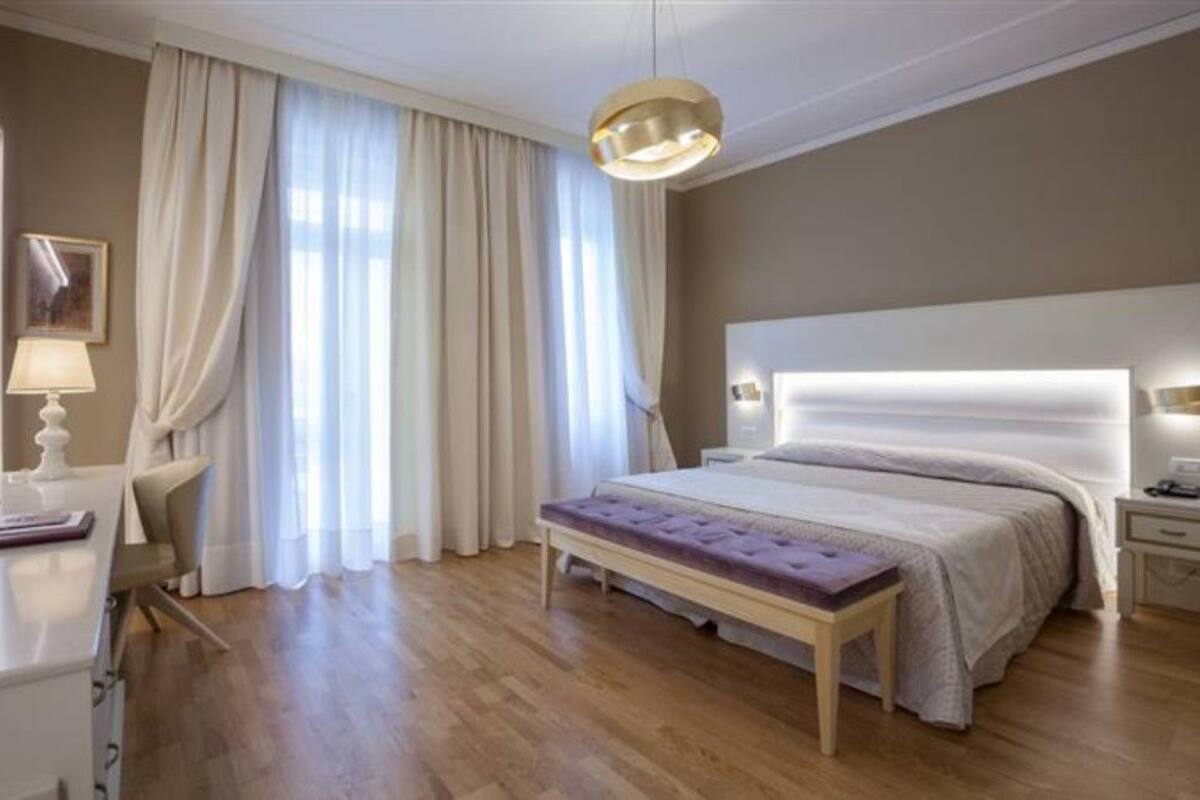 Een moderne slaapkamer met een groot bed, nachtkastjes, een bankje en een hanglamp.