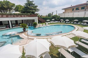 A swimming pool with lounge chairs and umbrellas, a waterfall feature, and a building with a modern design. - Hotel Quisisana (Abano Terme)