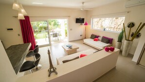 A modern living room with a sofa, a coffee table, and a TV. There is a dining area with chairs and a table. - Villas Agua Dulce - Loft Panaema (Sosúa)
