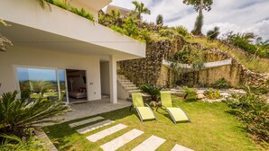 Una casa moderna con un patio amplio, mobiliario exterior y una escalera que lleva a un balcón.