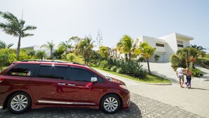 Una minivan roja estacionada frente a un edificio moderno blanco con un jardín ajardinado.