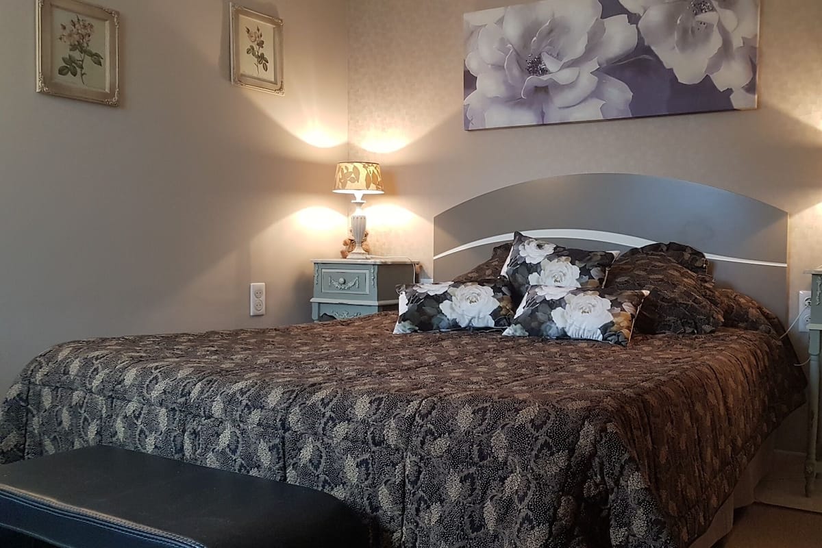 Ein Schlafzimmer mit einem großen Bett, zwei Nachttischen, einer Bank und einer Wanddekoration mit floralem Muster.