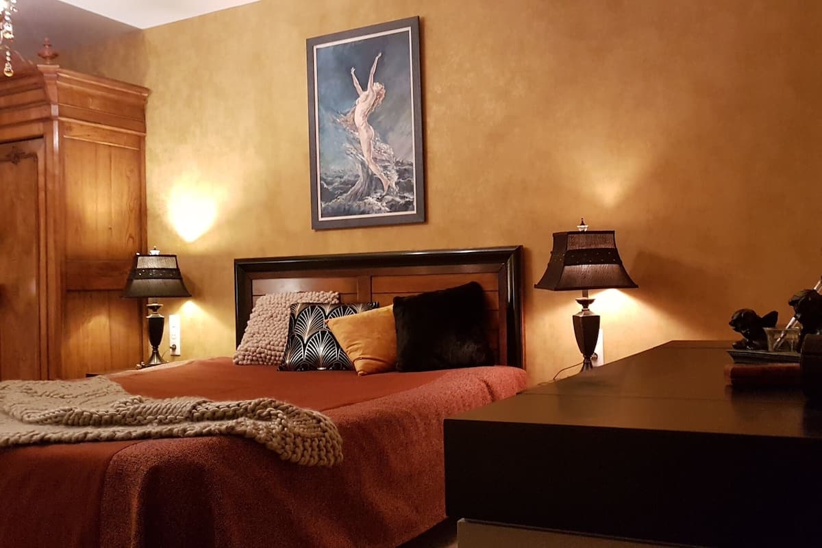 Ein Hotelzimmer mit einem Bett, zwei Nachttischlampen, einem Nachttisch, einer Zimmerpflanze und einem gerahmten Bild an der Wand.