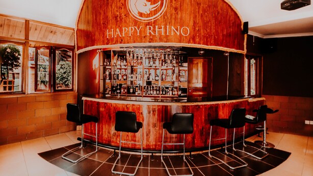 Uma área de bar com balcão curvo de madeira, banquetas e um letreiro com a inscrição 
