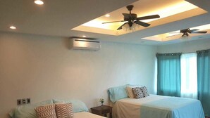 A hotel room with two beds, ceiling fans, an air conditioning unit, and a window with curtains. - West End room (Roatan)