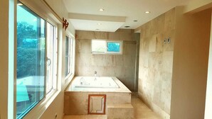 A modern bathroom with a large bathtub, a window, and a shower area. - West End room (Roatan)