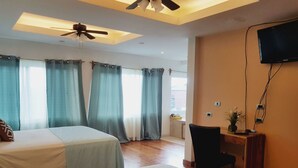 A hotel room with two beds, a desk, a chair, a ceiling fan, and a TV mounted on the wall. - West End room (Roatan)