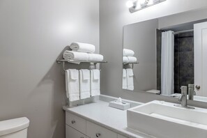 A bathroom with a white sink, a mirror, a towel rack with folded towels, and a toilet. - Motel 6 Merritt BC (Merritt)