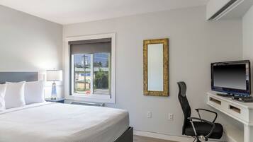 A hotel room with a bed, a desk with a computer, a chair, a TV, and a window with a view of buildings and a stop sign.