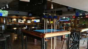 A billiards table with stools, a bar area, and multiple TVs in a dimly lit indoor space. - Motel 6 Merritt BC (Merritt)