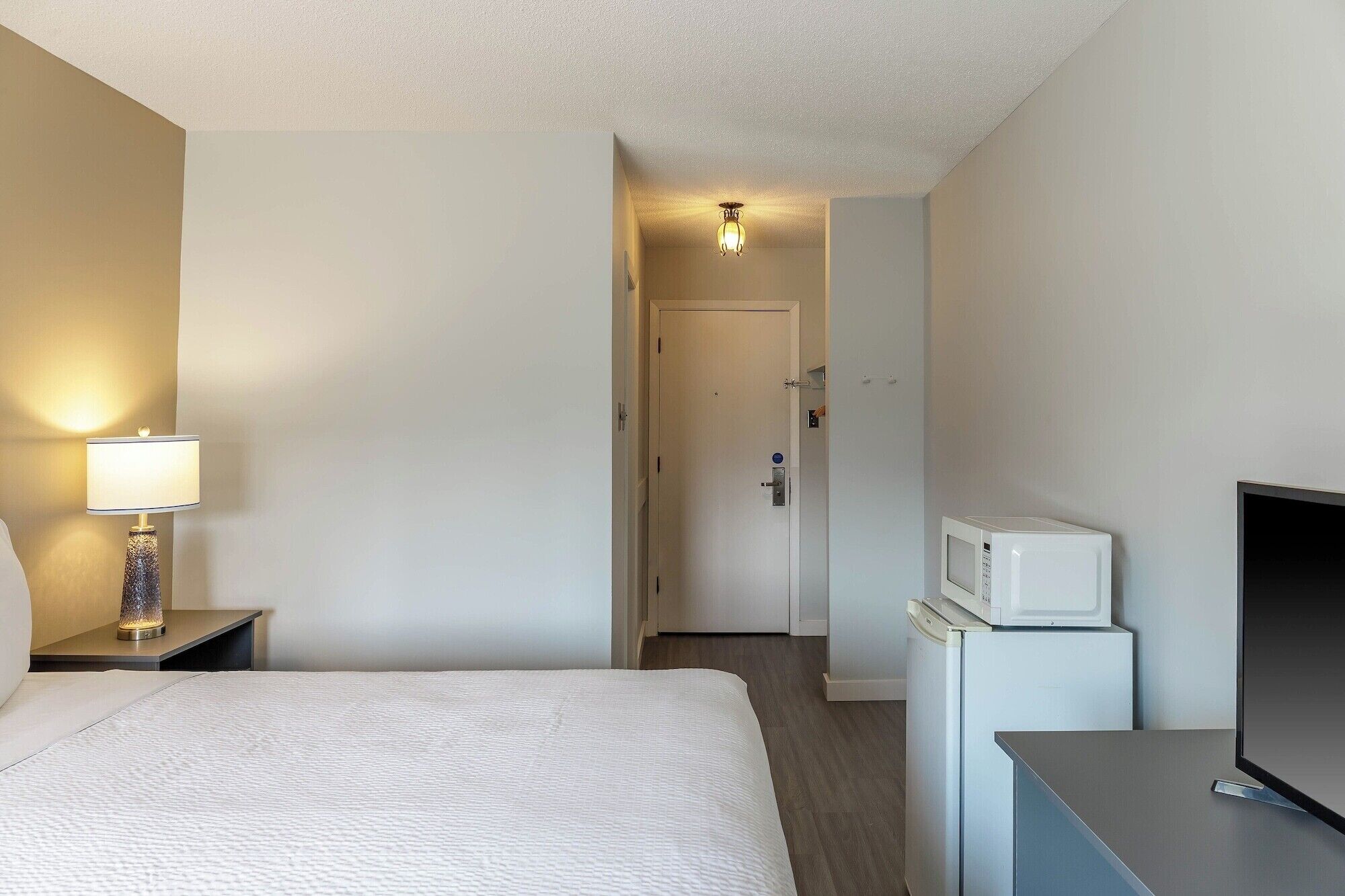 Une chambre d’hôtel équipée d’un lit, d’une télévision, d’un four à micro-ondes et d’une table de chevet avec une lampe.