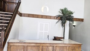 A reception desk with a wooden finish, a white door, a staircase, and a potted palm plant. - Motel 6 Merritt BC (Merritt)
