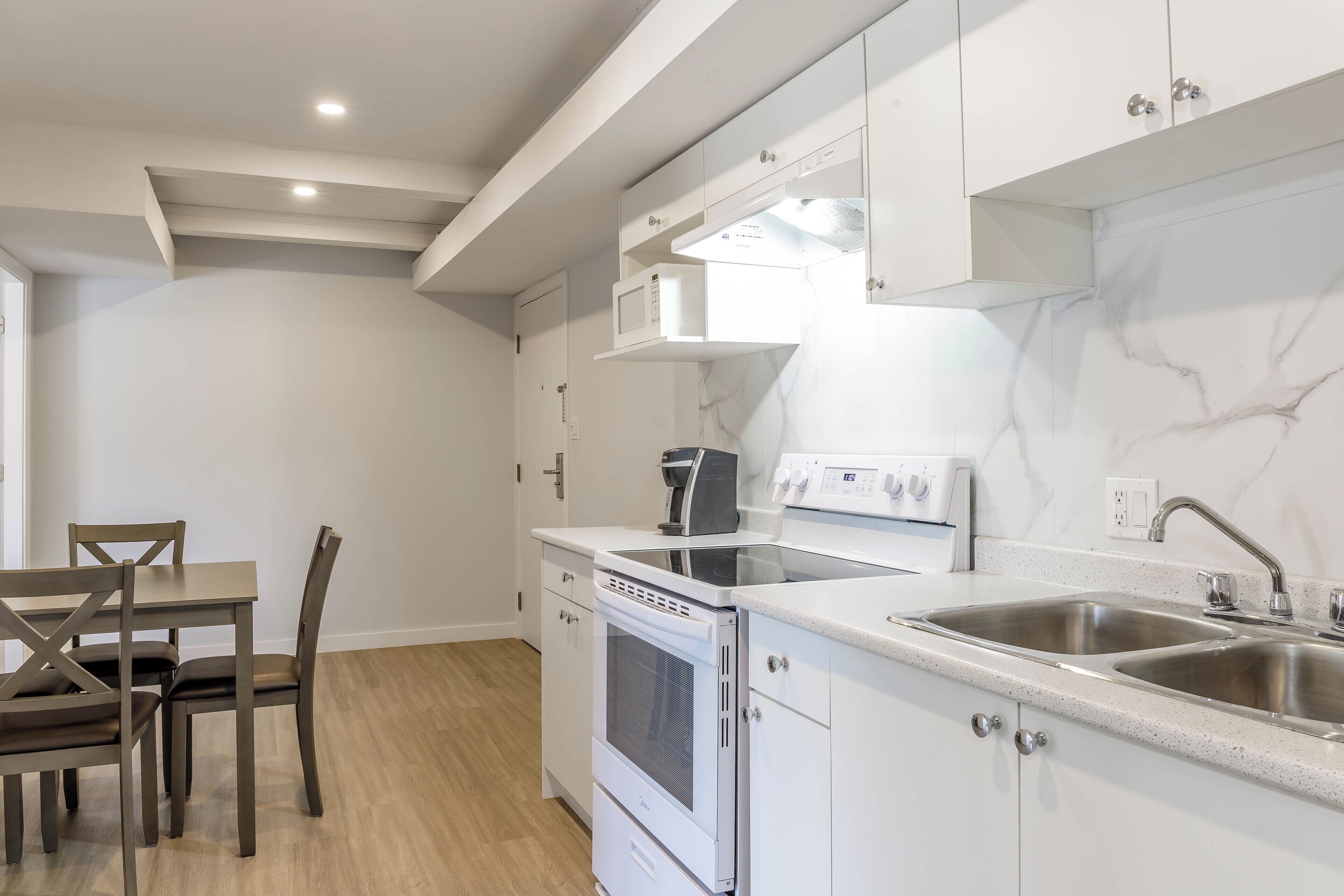 A modern kitchen with white cabinets, a built-in oven, a microwave, and a stainless steel sink.