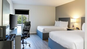 A hotel room with a desk, a chair, a bed, a TV, and a window with a view of trees. - Motel 6 Merritt BC (Merritt)