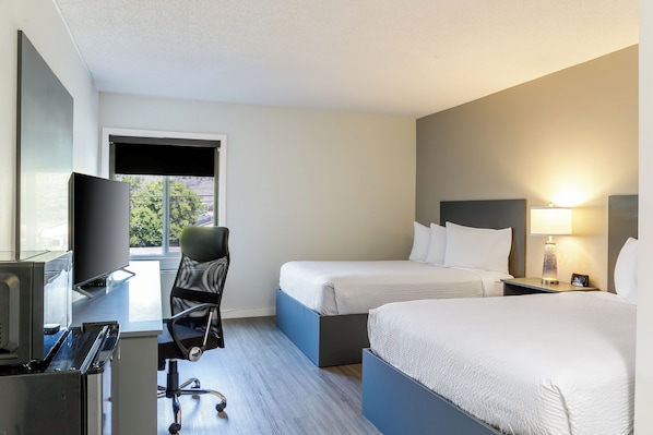 A hotel room with a desk, a chair, a bed, a TV, and a window with a view of trees.