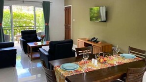 A dining area with a table set for two, a sofa, and a TV mounted on the wall. - Anse La Mouche Holiday Apartments (Victoria)
