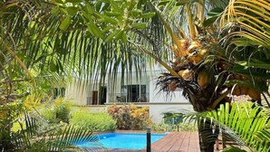 A pool area with a wooden deck, surrounded by lush greenery and palm trees. - Anse La Mouche Holiday Apartments (Victoria)