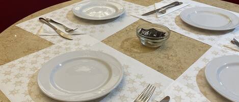 A table set with white plates, cutlery, and napkins on a patterned tablecloth.