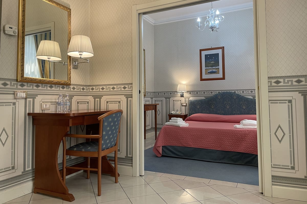 A hotel room with a desk, chair, bed, and a large mirror.