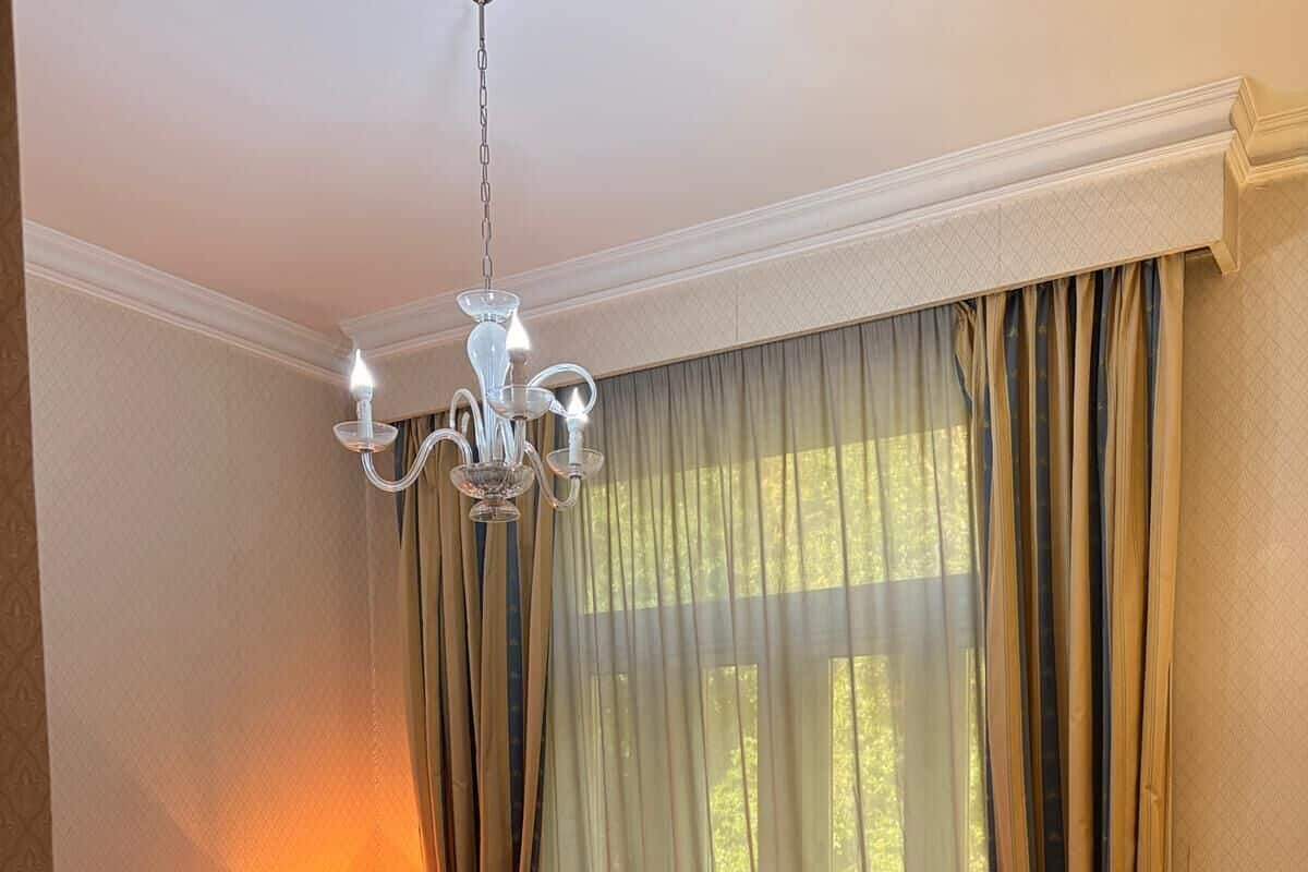 A hotel room with a bed, a table, a lamp, and a chandelier.