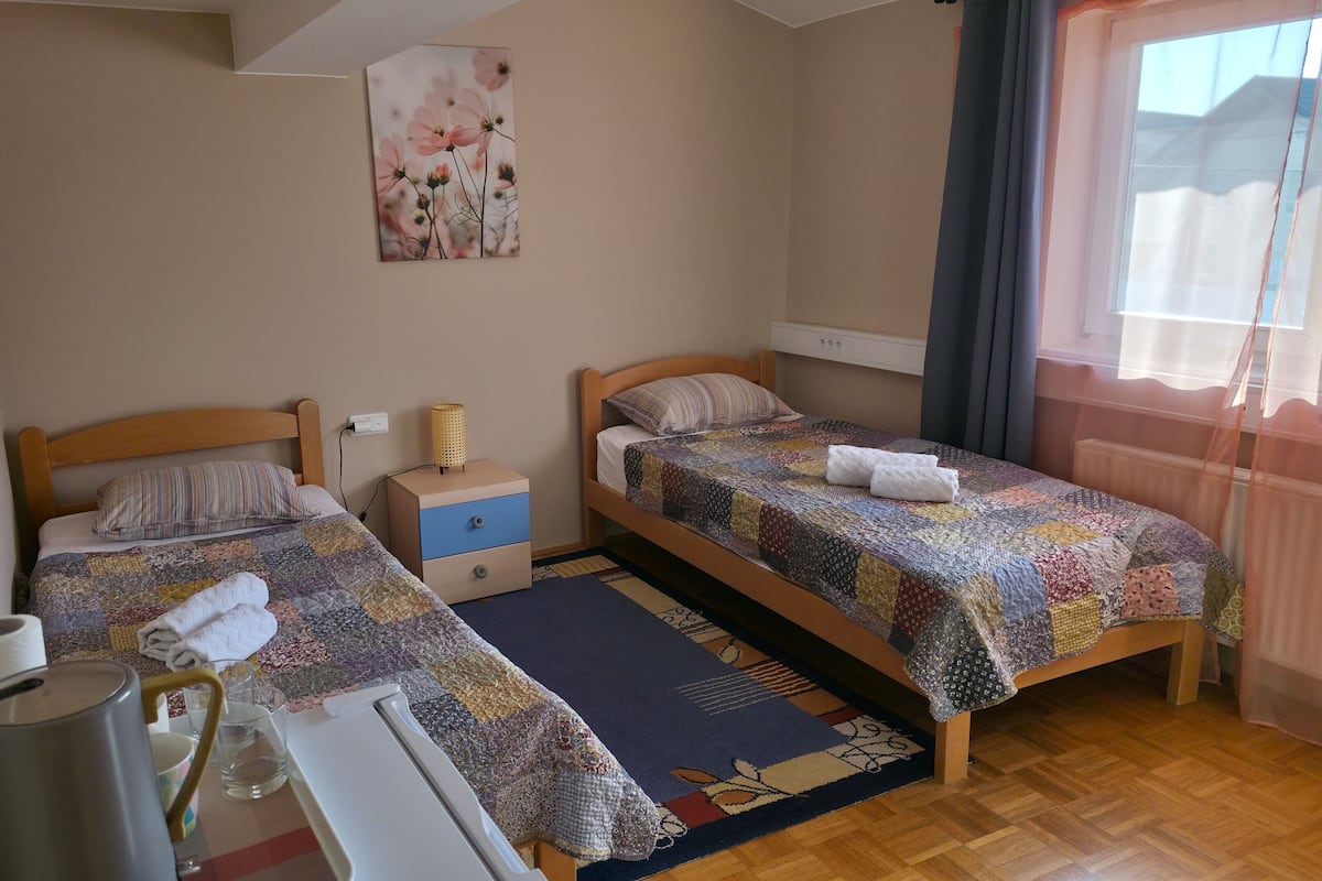 Et soveværelse med to senge, et natbord, en lampe, et maleri og et vindue med gardiner.