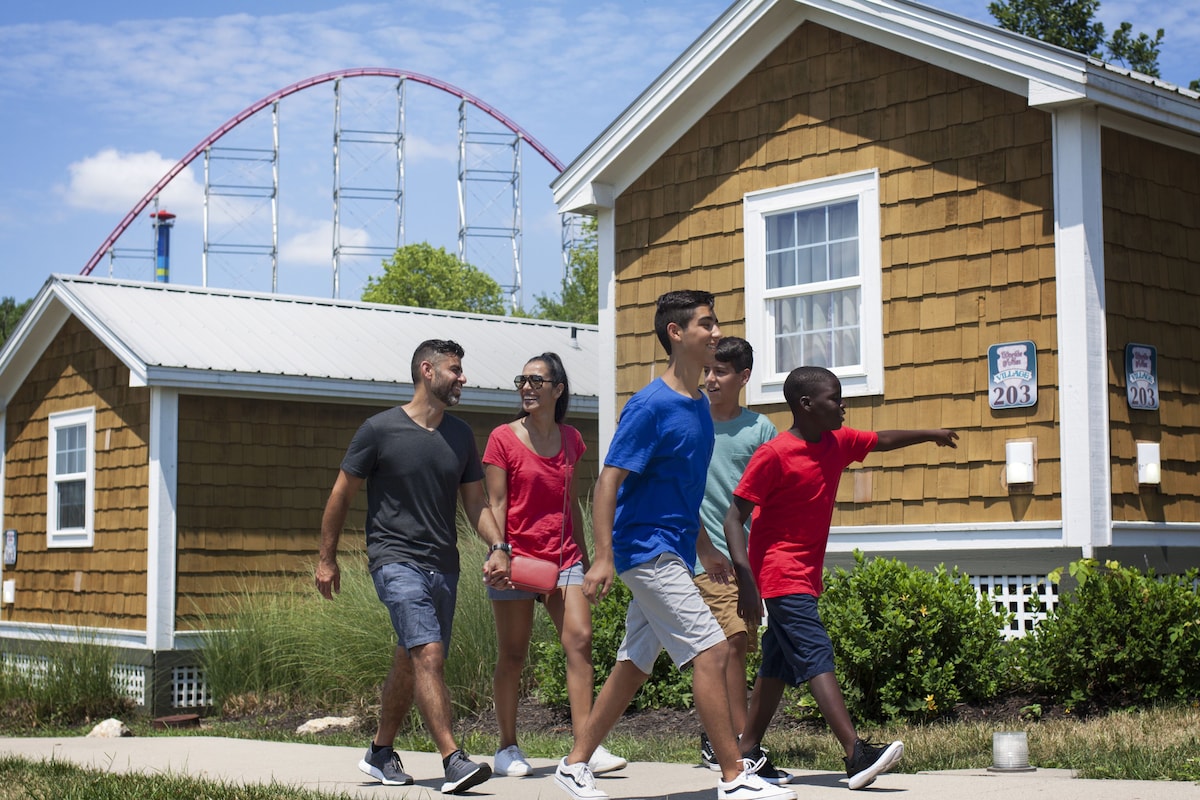 A group of people walking in front of a house with a roller coaster in the background.