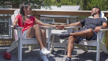 Two people seated on white chairs on a wooden deck, holding hands.