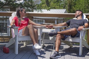 Two people seated on white chairs on a wooden deck, holding hands.
