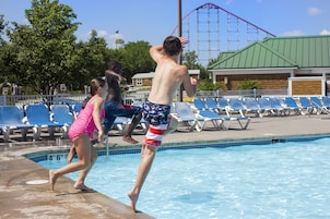 A swimming pool with a water slide and a roller coaster in the background.