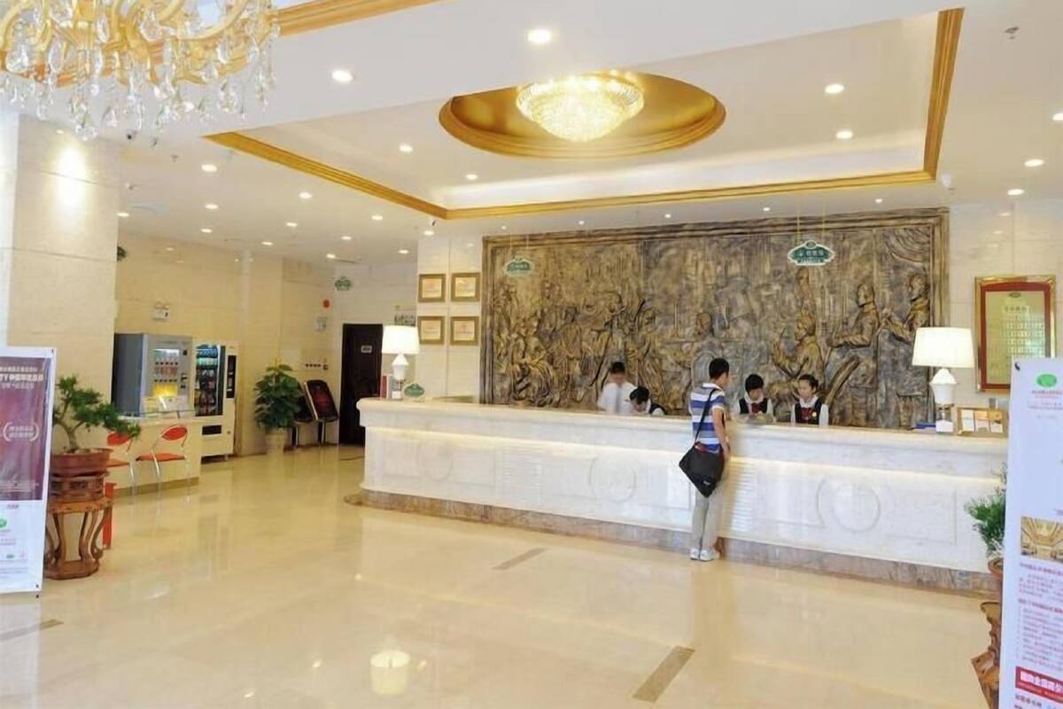 A hotel reception area with a marble reception desk, a chandelier, and a large wall mural.