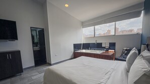 A modern hotel room with a large bed, a desk with a chair, a TV mounted on the wall, and a view of the city through the window. - Provenza Lofts (Medellín)