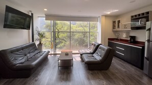 A modern living room with leather sofas, a coffee table, and a large window with a view of trees. - Provenza Lofts (Medellín)