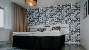 Ein Schlafzimmer mit einem Bett, einer Kopfteil, einem Fenster mit Vorhängen und blumigem Wandpapier.