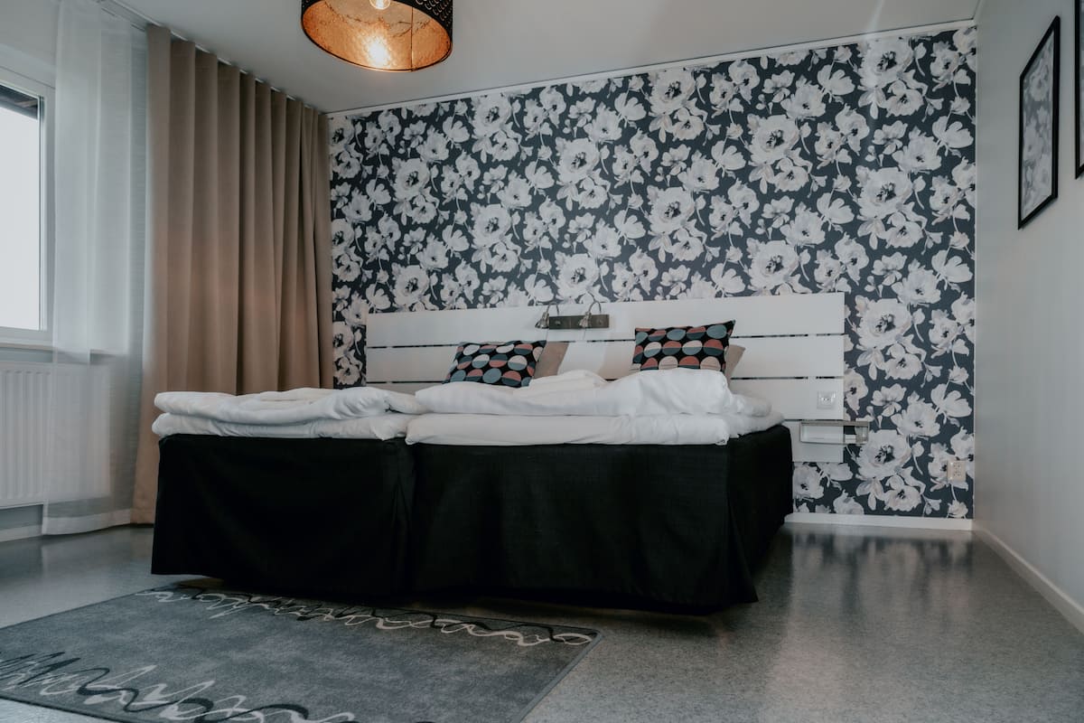 A bedroom with a bed, a headboard, a window with curtains, and a floral wallpaper.