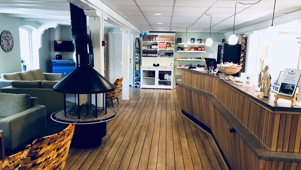 Eine Hotelhalle mit Holzboden, einer Rezeption, einer Sitzecke mit Sofa und Sesseln sowie einem an der Wand befestigten Fernseher.