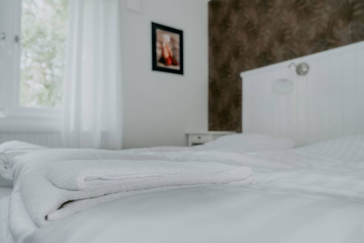 A neatly made bed with white linens, a white headboard, and a framed picture on the wall.